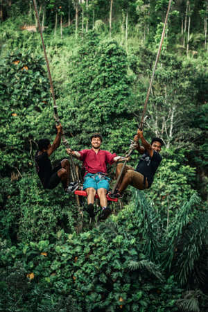 BALI, INDONESIA - MAY 16, 2018: Young man swinging in the jungle rainforest of Bali island, Indonesia. Swing in the tropics. Swings - trend of Bali island.のeditorial素材