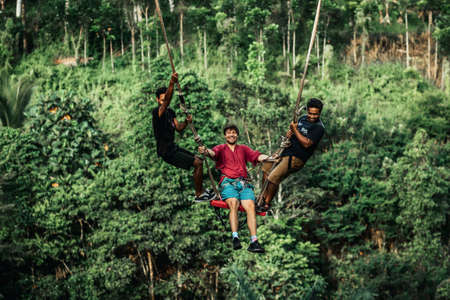 BALI, INDONESIA - MAY 16, 2018: Young man swinging in the jungle rainforest of Bali island, Indonesia. Swing in the tropics. Swings - trend of Bali island.のeditorial素材