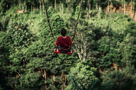Young man swinging in the jungle rainforest of Bali island, Indonesia. Swing in the tropics. Swings - trend of Bali island.の写真素材