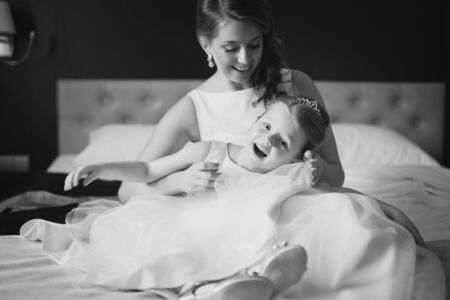 Mother and daughter in the same wedding dresses having fun on the bedの写真素材