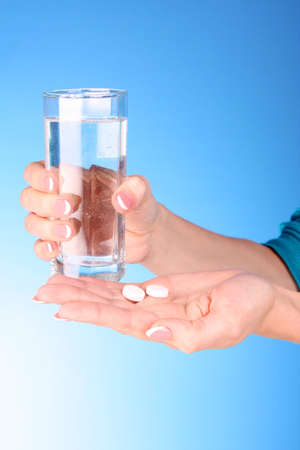 Tablets and glass of water in the woman hands on blue backgroundの写真素材