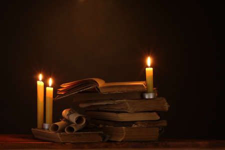 Pile of old books with candle and scroll in darkの写真素材