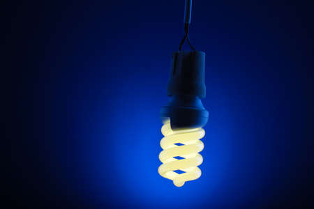 A lit energy saving light bulb on blue backgroundの写真素材
