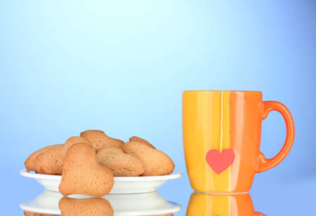 Heart-shaped cookies on plate and cup with tea bag on blue backgroundの写真素材