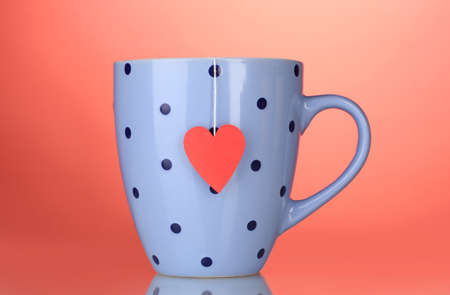 Blue cup and tea bag with red heart-shaped label on red backgroundの写真素材