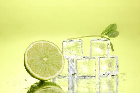 Fresh mint leaf and ice cubes with droplets and lime on green backgroundの写真素材