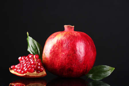 ripe pomegranate fruit with leaves on black backgroundの写真素材