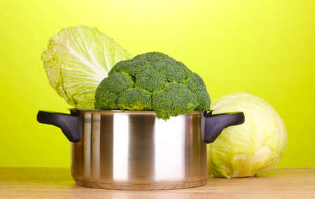 Saucepan with broccoli and cabbages on wooden table on green backgroundの写真素材