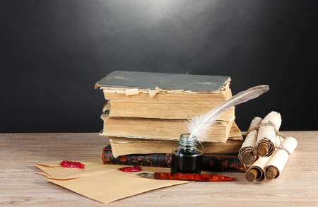 old books, scrolls, feather pen and inkwell on wooden table on grey backgroundの写真素材