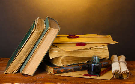 old books, scrolls, ink pen and inkwell on wooden table on brown backgroundの写真素材