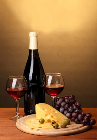 Bottle of great wine with wineglasses and cheese on wooden table on brown backgroundの写真素材