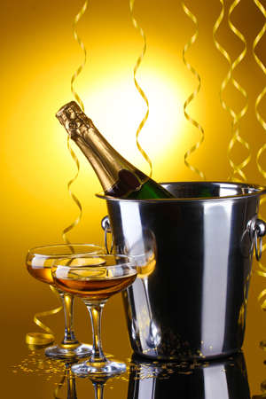 Champagne bottle in bucket with ice and glasses of champagne, on yellow backgroundの写真素材