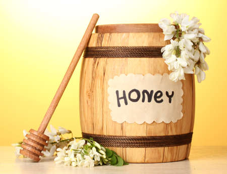 Sweet honey in barrel with acacia flowers on wooden table on yellow backgroundの写真素材