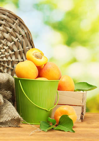 bucket and wooden box with ripe apricots on wooden table on green backgroundの写真素材