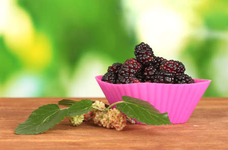 Bright silicone cutter with ripe mulberry on wooden table on bright green background close-upの写真素材