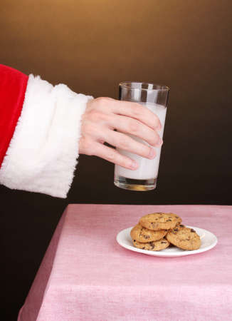 Santa Claus hand holding glass of milk on brown backgroundの写真素材