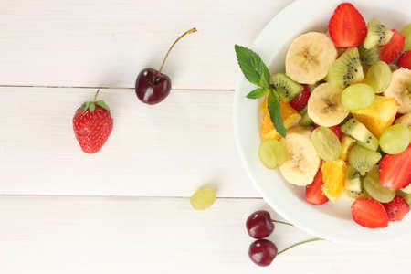 Fresh fruits salad on plate and berries on white wooden tableの写真素材