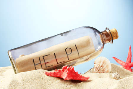 Glass bottle with note inside on sand, on blue backgroundの写真素材