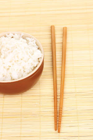 Bowl of rice and chopsticks on bamboo matの写真素材