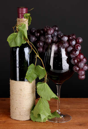 bottle of wine with grape leaves on wooden table on black backgroundの写真素材