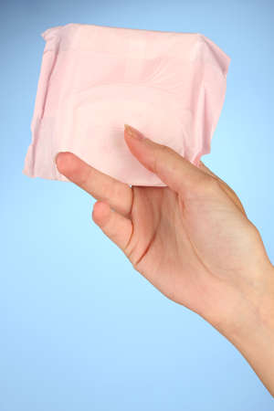 woman's hand holding a panty liner in individual packing on blue background close-upの写真素材