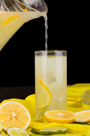 Citrus lemonade in glass and pitcher of citrus around on yellow fabric on wooden table close-upの写真素材