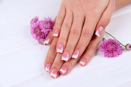 Woman hands with french manicure and flowers on white wooden backgroundの写真素材