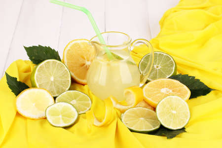 Citrus lemonade in glass pitcher of citrus around on yellow fabric on white wooden table close-upの写真素材