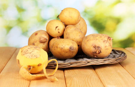 Ripe potatoes on wicker cradle on wooden table on natural backgroundの写真素材