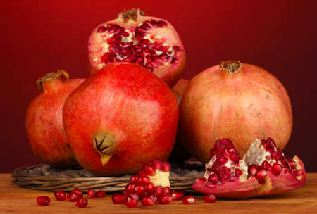 Ripe pomegranates on wicker cradle on red backgroundの写真素材