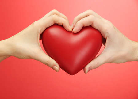 Red heart in woman and man hands, on red backgroundの写真素材