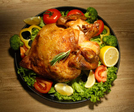 Whole roasted chicken with vegetables on plate, on wooden tableの写真素材