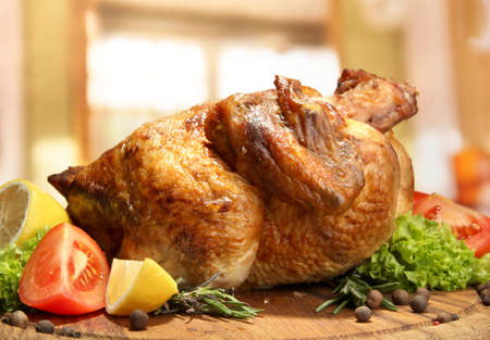 Whole roasted chicken with vegetables on plate, on wooden table in cafeの写真素材