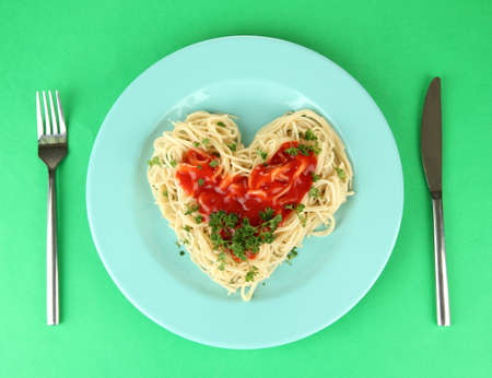 Cooked spaghetti carefully arranged in  heart shape and topped with tomato sauce, on color backgroundの写真素材