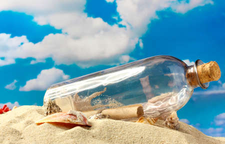 Glass bottle with note inside on sand, on blue sky backgroundの写真素材