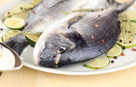 Two fish dorado with lemon on plate on wooden table close-upの写真素材
