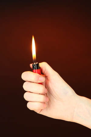 Burning lighter in female hand, on dark brown backgroundの写真素材