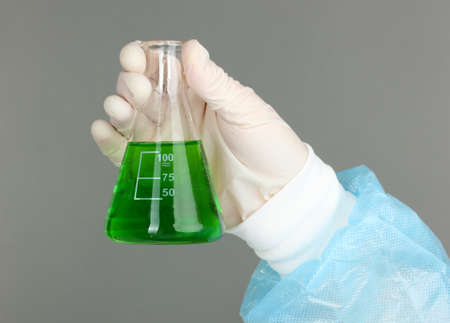 Glass tube with fluid in scientist hand during medical test on grey backgroundの写真素材