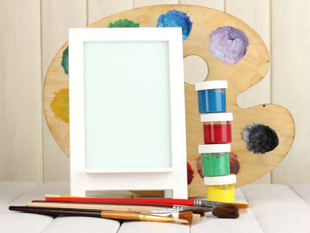 Photo frame as easel with artist's tools on wooden backgroundの写真素材