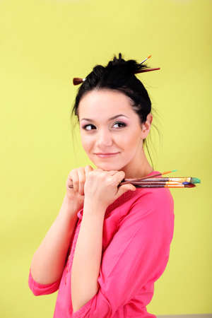 Beautiful young woman painter with brushes, on color backgroundの写真素材