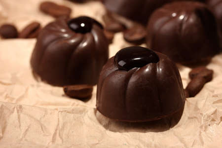 Chocolate candies and coffee beans, on beige paper backgroundの写真素材