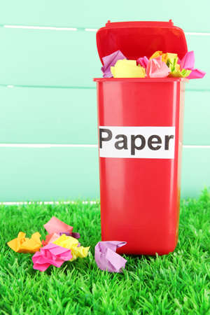 Recycling bin with papers on grass on light blue backgroundの写真素材