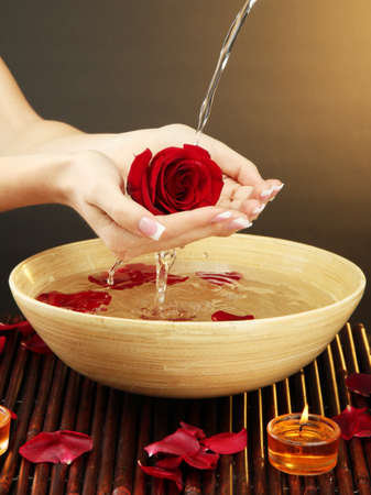 woman hands with wooden bowl of water with petals, on brown backgroundの写真素材