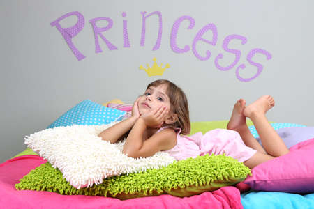 Little girl lying on bed in room on grey wall backgroundの写真素材