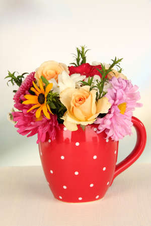 Beautiful bouquet of bright flowers in color mug, on wooden table, on  light backgroundの写真素材