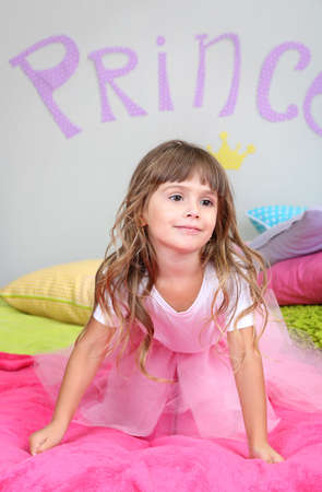 Little girl jumping on bed in room on grey wall backgroundの写真素材