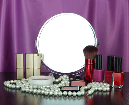 Round table mirror with cosmetics and chaplet on table on fabric backgroundの写真素材