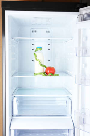 Conceptual photo of diet: apple and milk bottle with measuring type on shelf of refrigeratorの写真素材