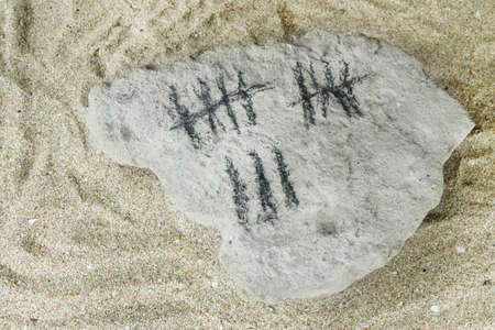 Counting days by drawing sticks on stone on sand backgroundの写真素材