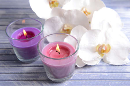 Beautiful colorful candles and  orchid flowers, on color wooden table, on light backgroundの写真素材